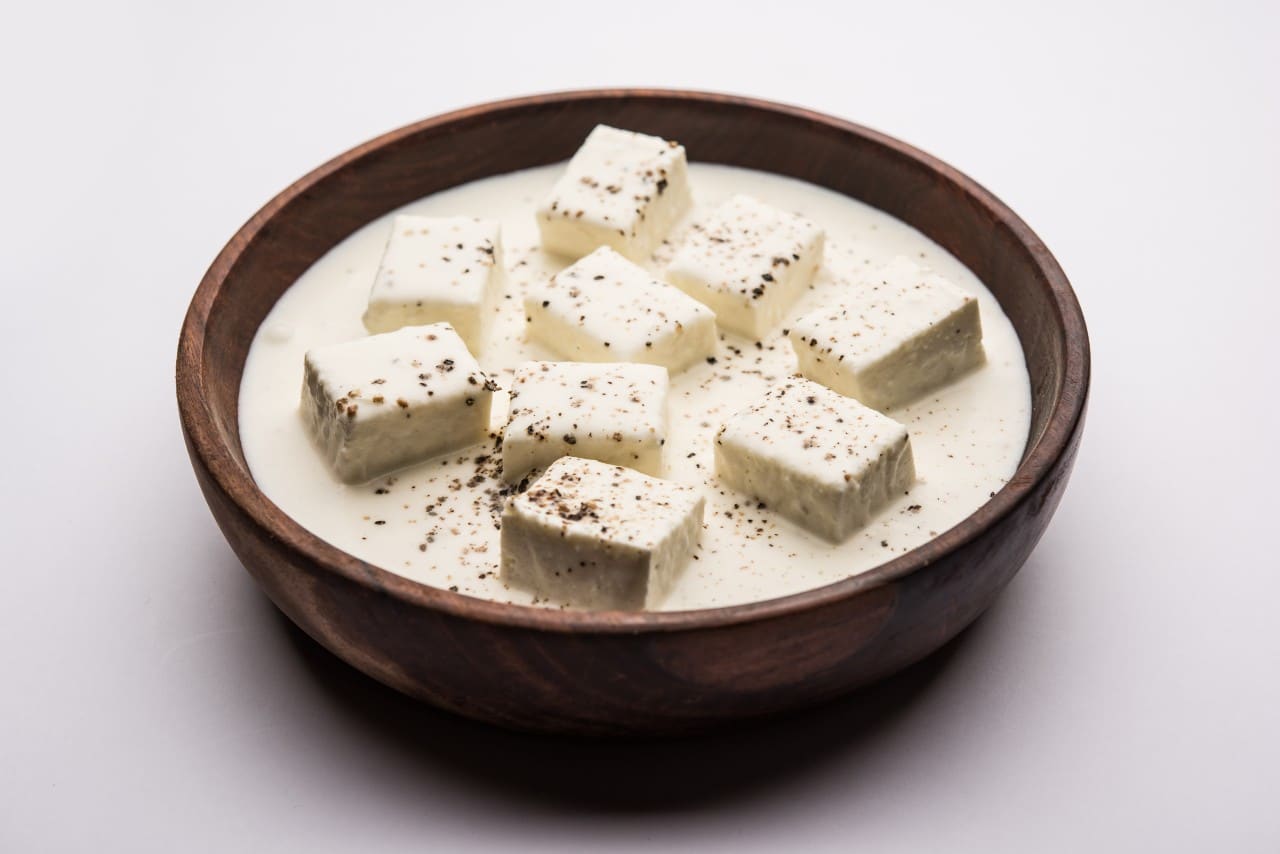 Delicious Malai Paneer cubes served in a wooden bowl with creamy white gravy and black pepper garnish