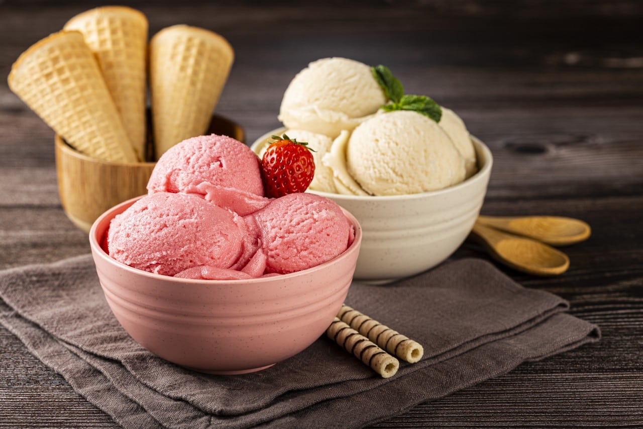 Delicious strawberry and vanilla ice cream scoops in bowls with waffle cones and wafer sticks on a rustic wooden table refreshing summer dessert