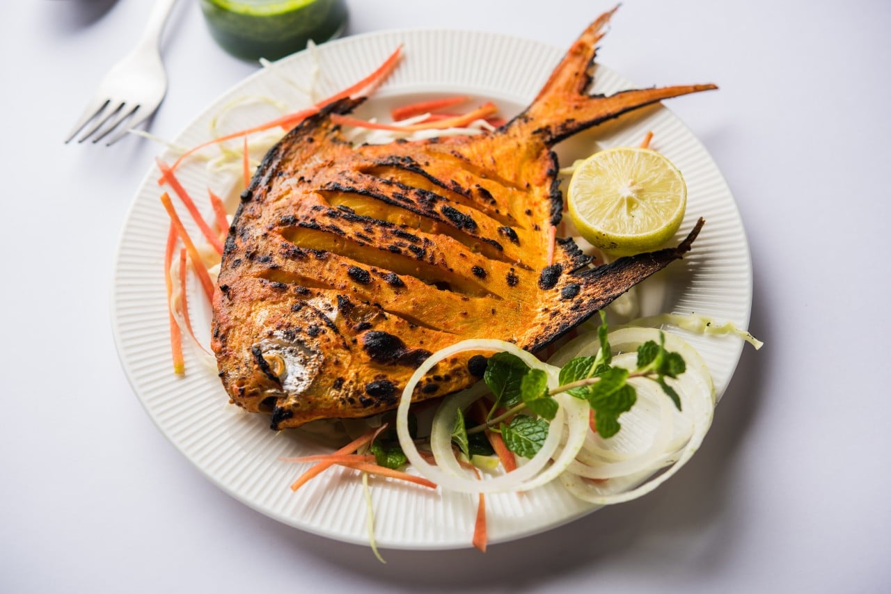 Grilled pomfret fish served with lemon onion rings and mint leaves on a white plate a popular Indian seafood dish
