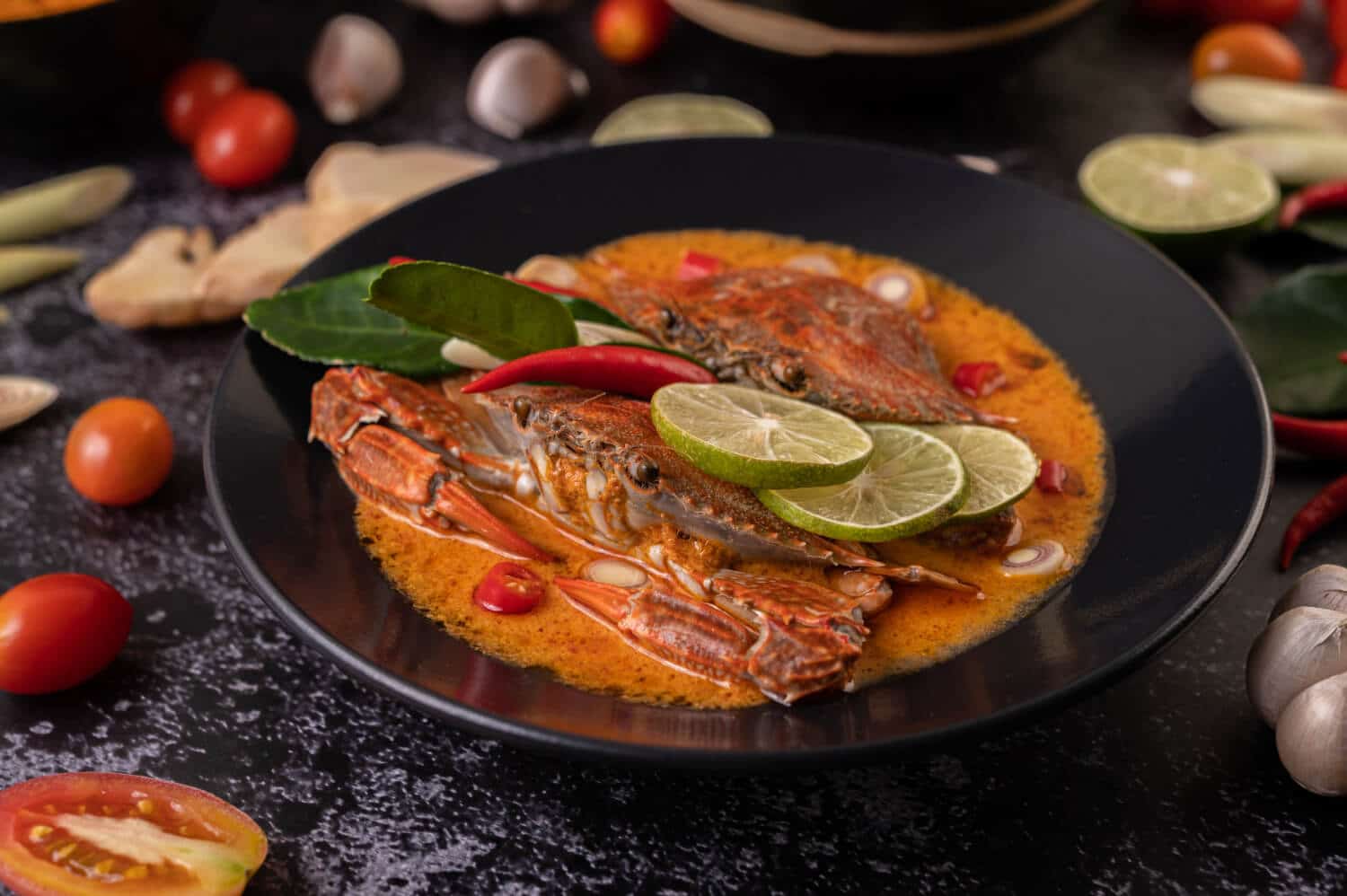 Which 25 Singapore Food Dishes Should You Try? 13 A black bowl of spicy red crab curry garnished with lime slices kaffir lime leaves and red chilies