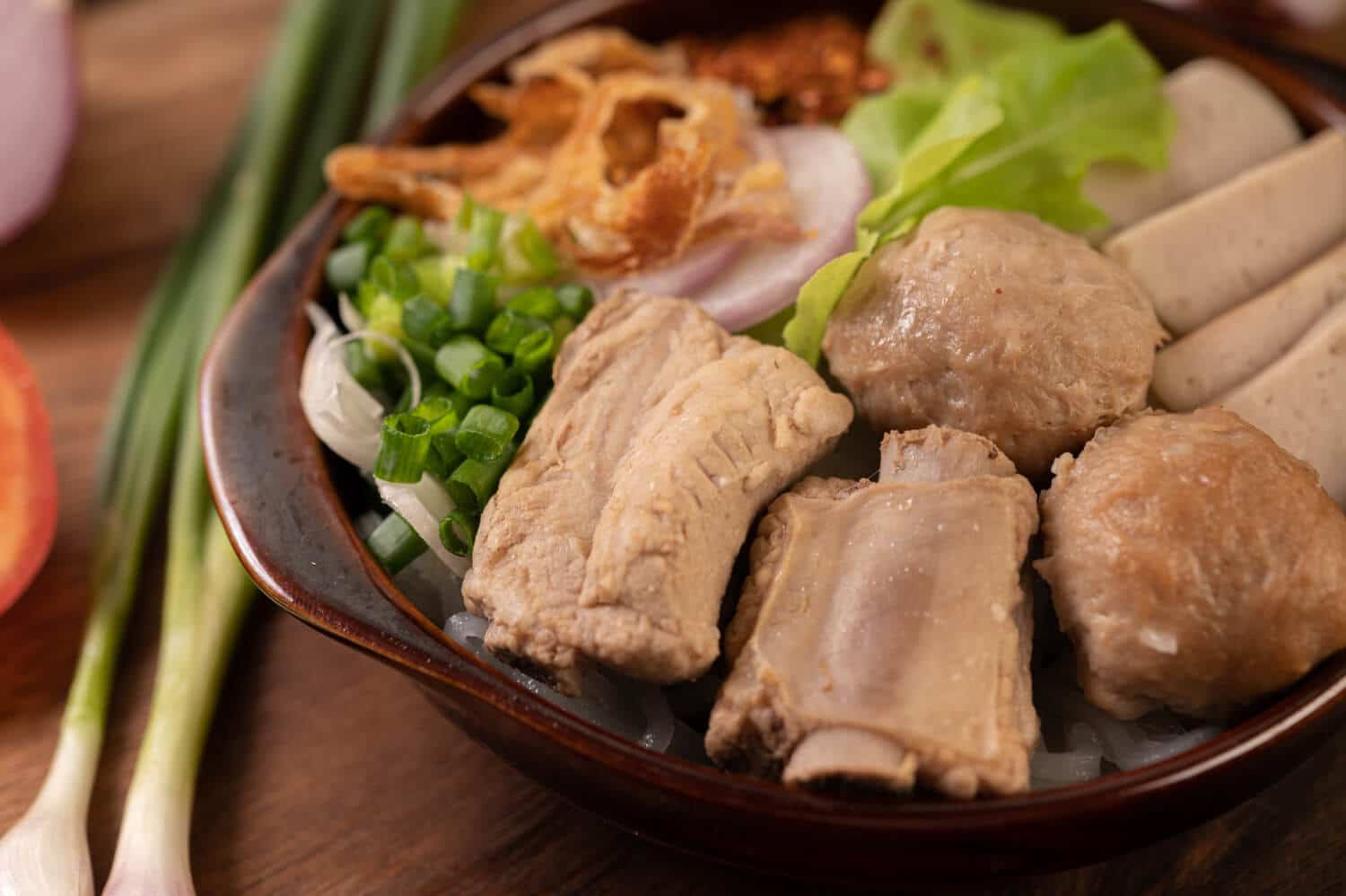 Which 25 Singapore Food Dishes Should You Try? 10 A close up of a noodle bowl topped with pork ribs large meatballs sliced pork roll crispy fried shallots