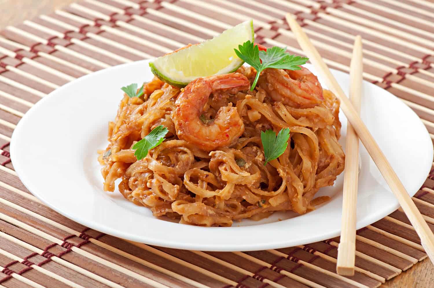Which 25 Singapore Food Dishes Should You Try? 16 A plate of Pad Thai with large shrimp garnished with a lime wedge and parsley
