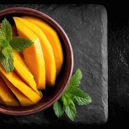 Which 15 Mango Varieties Should You Try This Summer? 48 Fresh sliced mangoes served in a bowl with mint leaves showcasing bright yellow pulp and summer fruit presentation