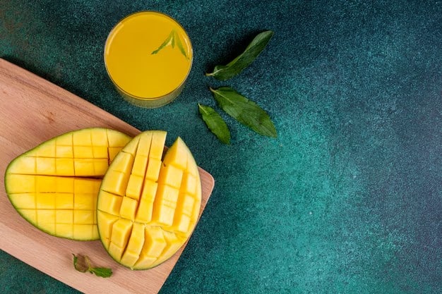 Sliced mango on a wooden board with a glass of mango juice and fresh mint leaves