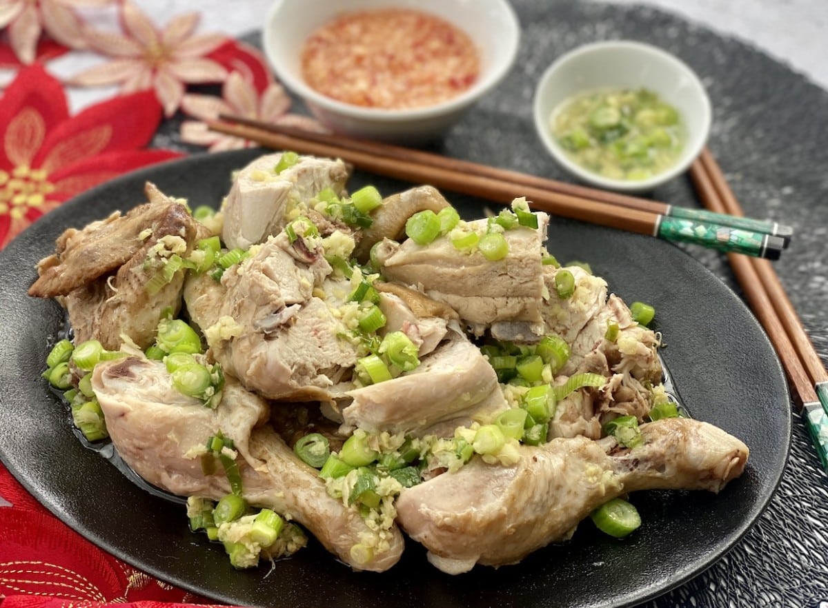 What Are 15 Chinese New Year Food Dishes You Must Try? 10 Steamed chicken pieces served on a black plate topped with chopped ginger and spring onions with dipping sauces and chopsticks placed alongside