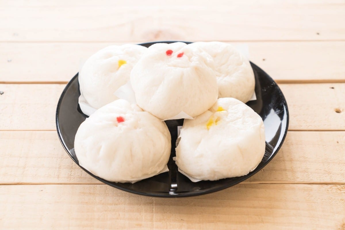 What Are 15 Chinese New Year Food Dishes You Must Try? 8 Steamed white buns arranged on a black plate served on a wooden surface showing soft round buns with lightly marked tops