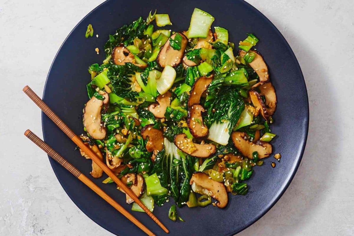 What Are 15 Chinese New Year Food Dishes You Must Try? 1 Stir fried mushrooms with bok choy served on a dark plate featuring sliced mushrooms leafy greens sesame seeds and garlic a traditional Chinese New Year vegetable dish