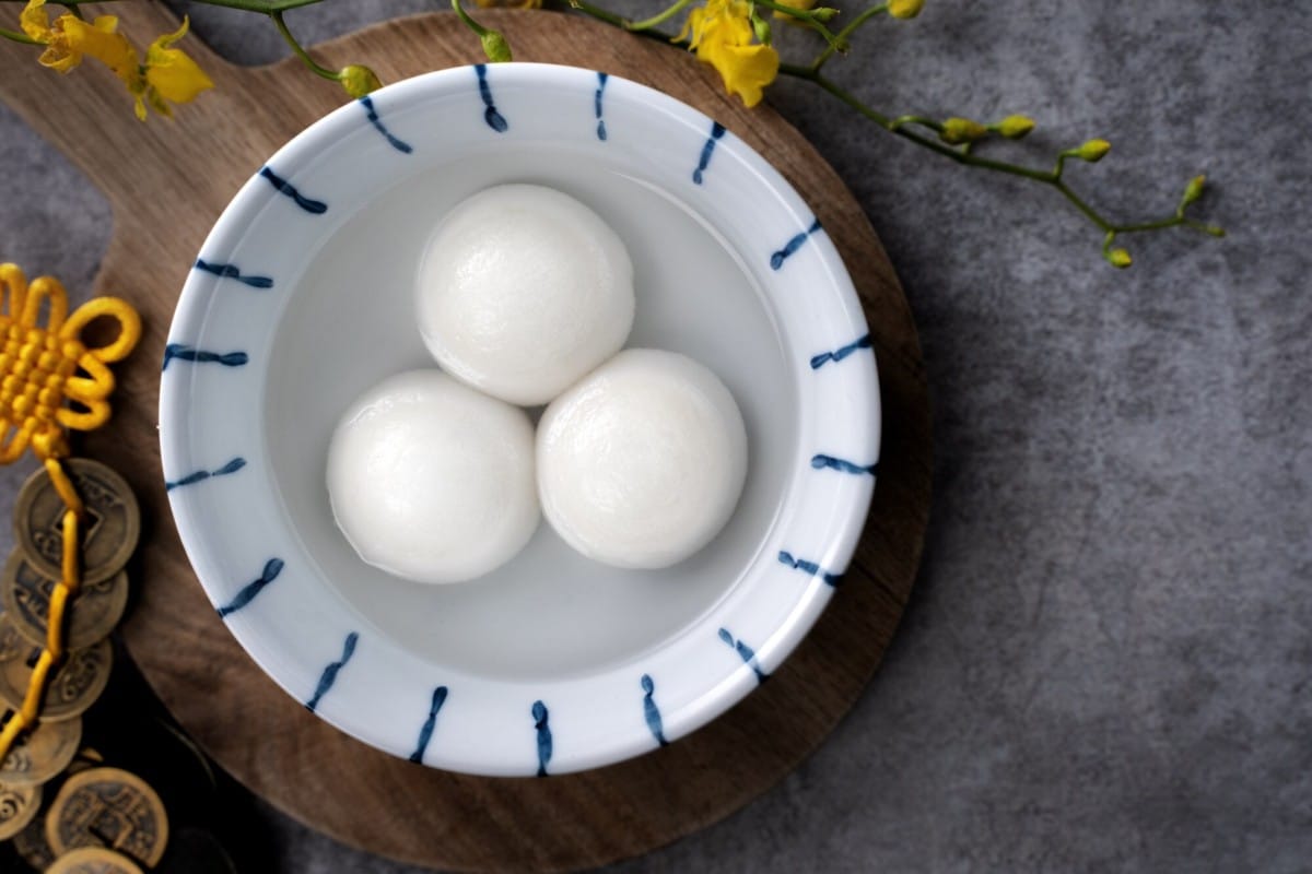 What Are 15 Chinese New Year Food Dishes You Must Try? 6 White sweet rice balls served in a bowl of clear syrup placed on a wooden board with decorative flowers and coins in the background