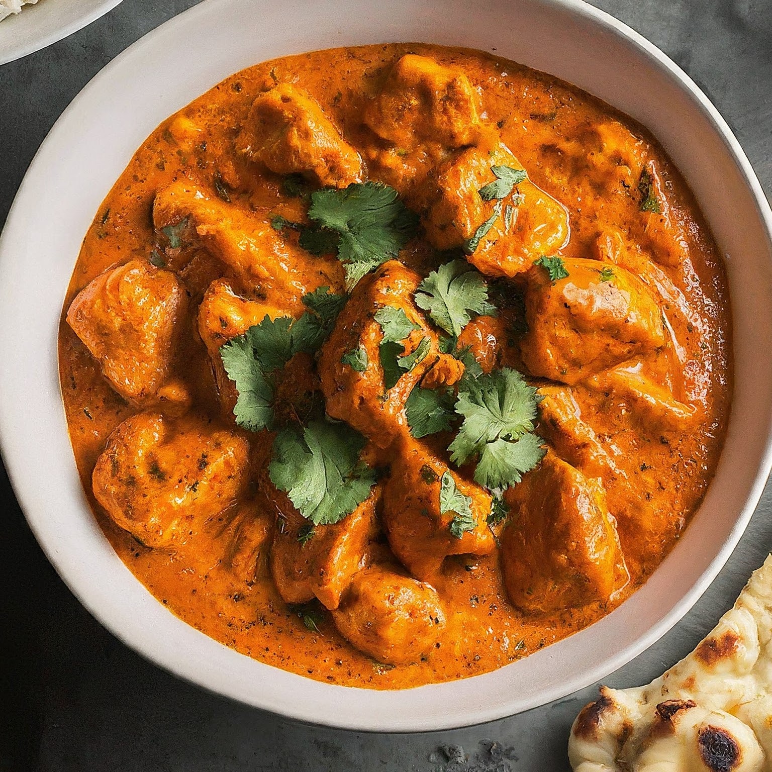 A delicious bowl of butter chicken with tender chicken in a creamy tomato sauce garnished with cilantro.