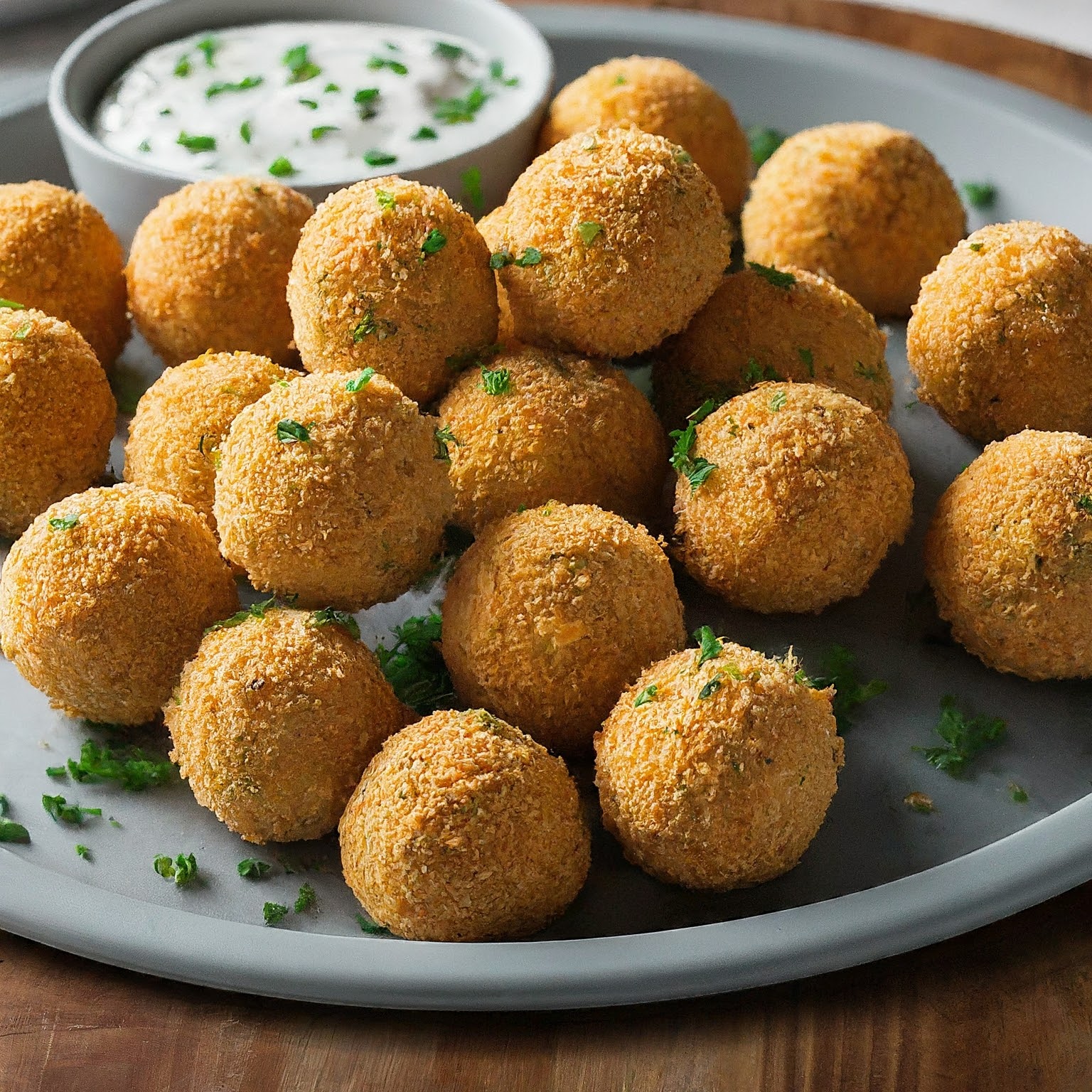 Platter of golden brown Cheesy Garlic Millet Balls with a creamy garlic sauce and fresh herbs.