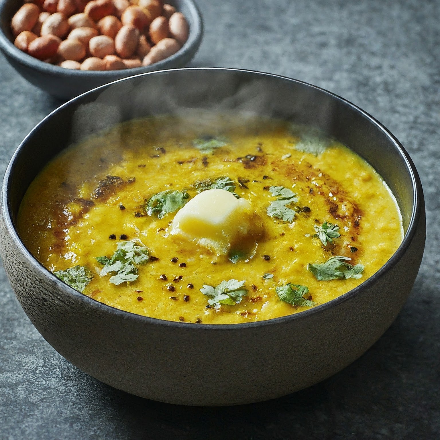 A steaming bowl of Gujarati Dal, a creamy lentil stew garnished with coriander and ghee, with roasted peanuts on the side.