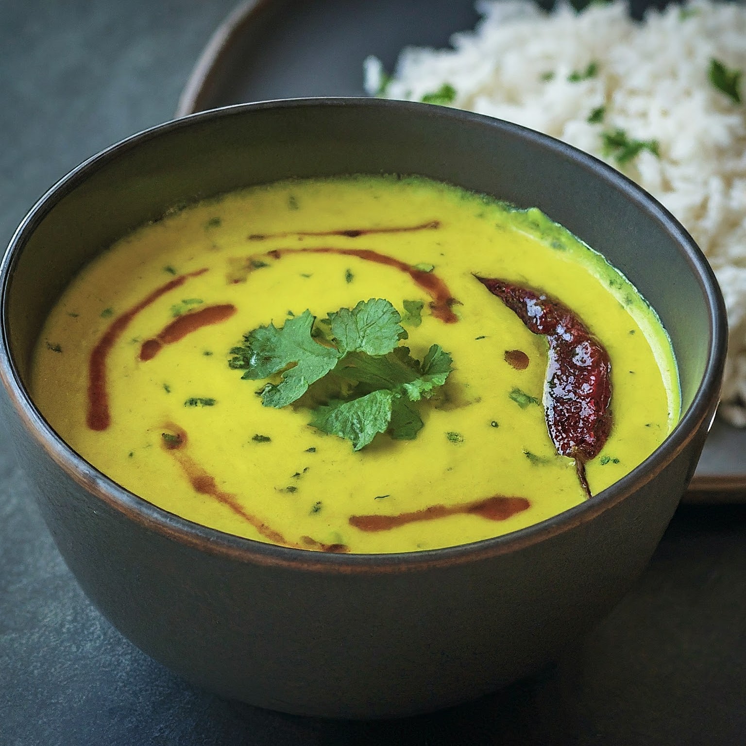 A bowl of Gujarati Kadhi, a vibrant yellow yoghurt curry with rice.