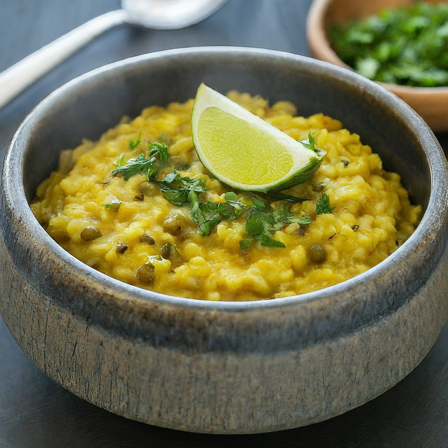 A steaming bowl of Moong Dal Khichdi, a lentil and rice dish garnished with cilantro and lime.