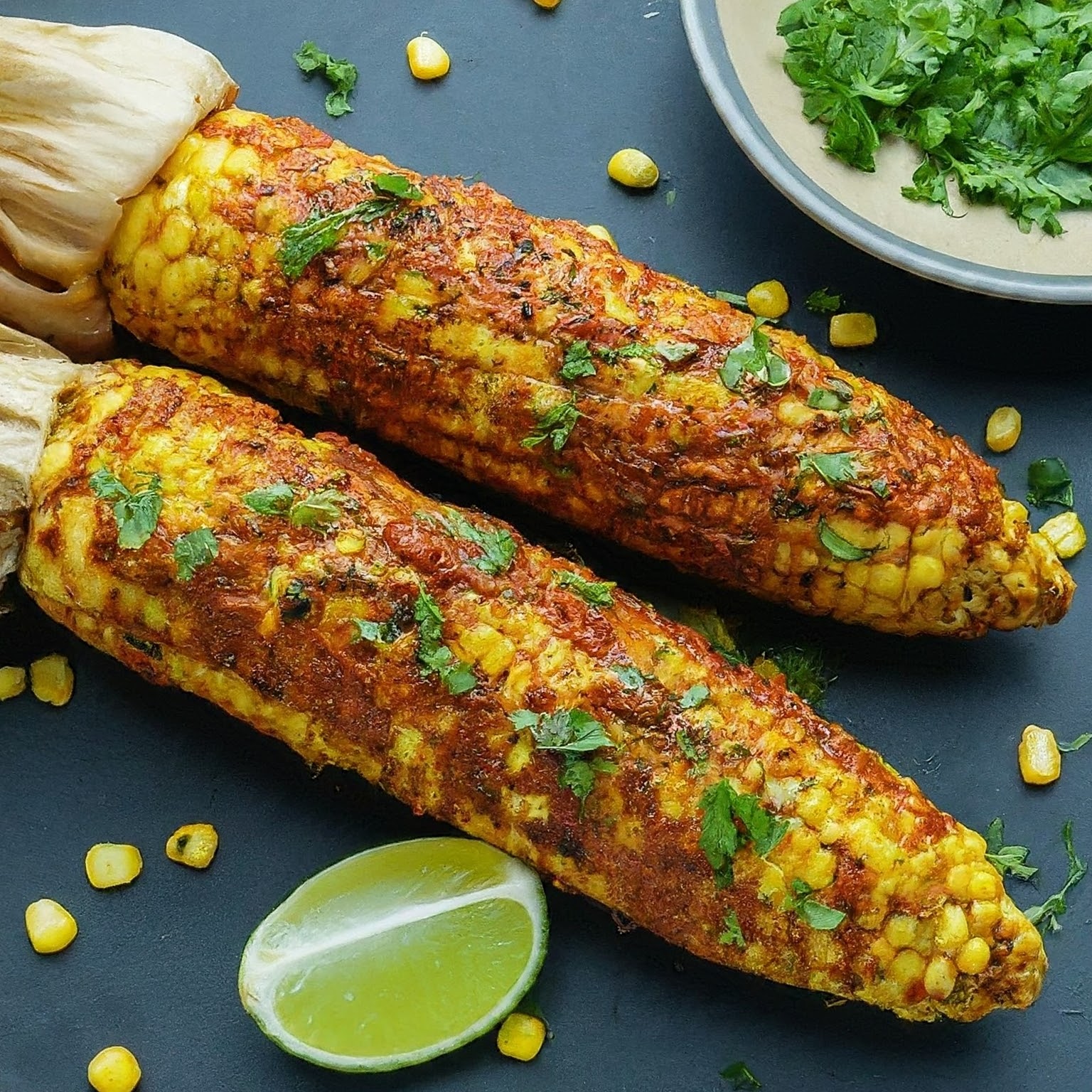 Steaming cob of corn coated in colourful masala paste, ready to be devoured.