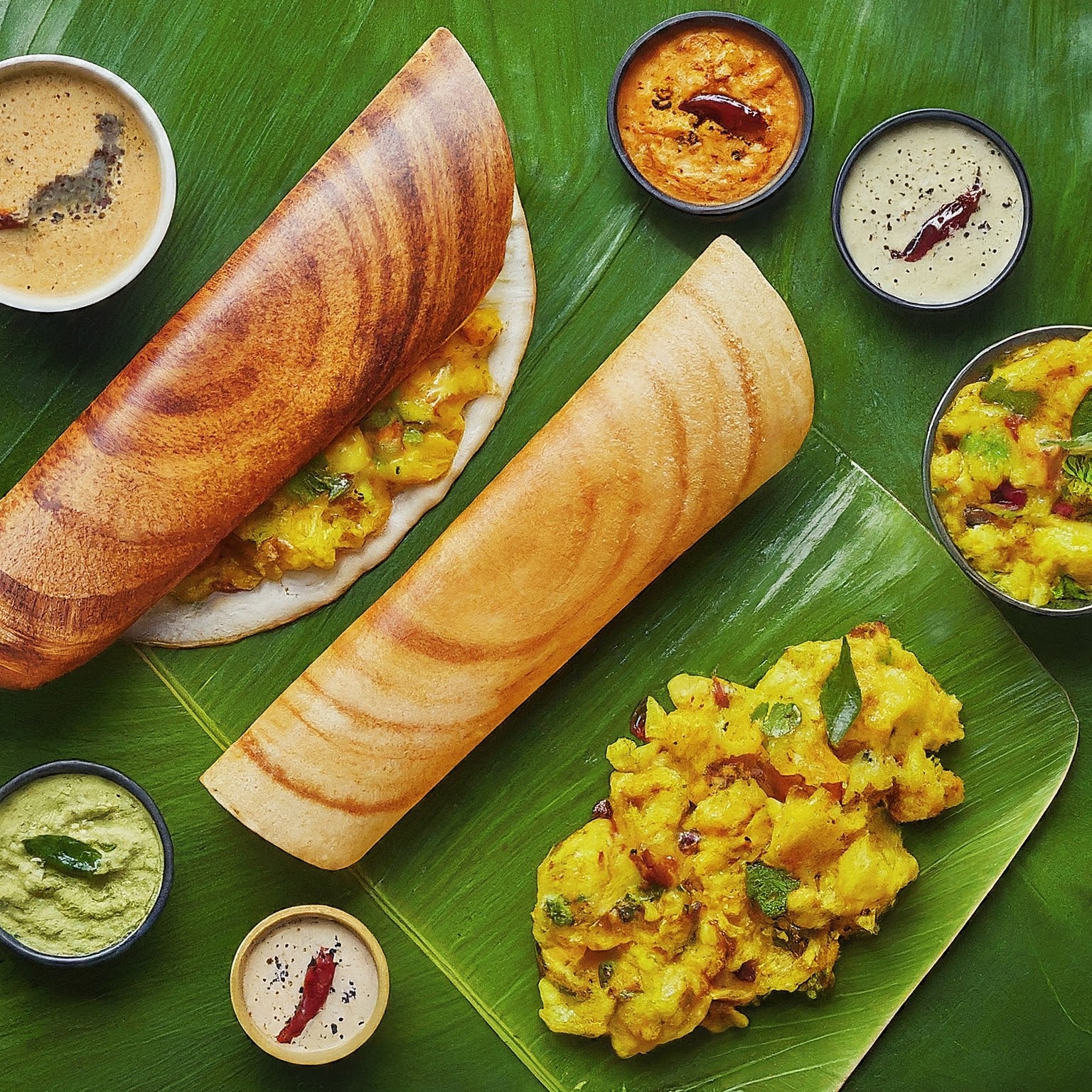 A delicious masala dosa served with coconut chutney and sambar on a banana leaf