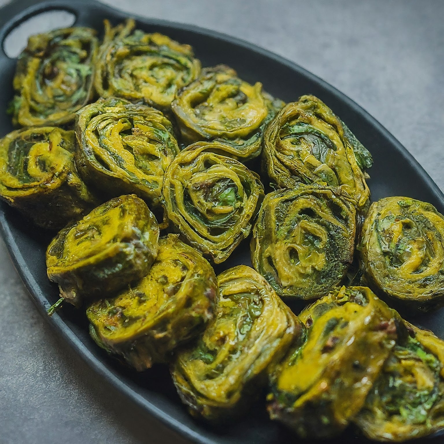 A close-up view of a plate of Patra, a green vegetarian dish with colocasia leaves and chickpea flour batter.