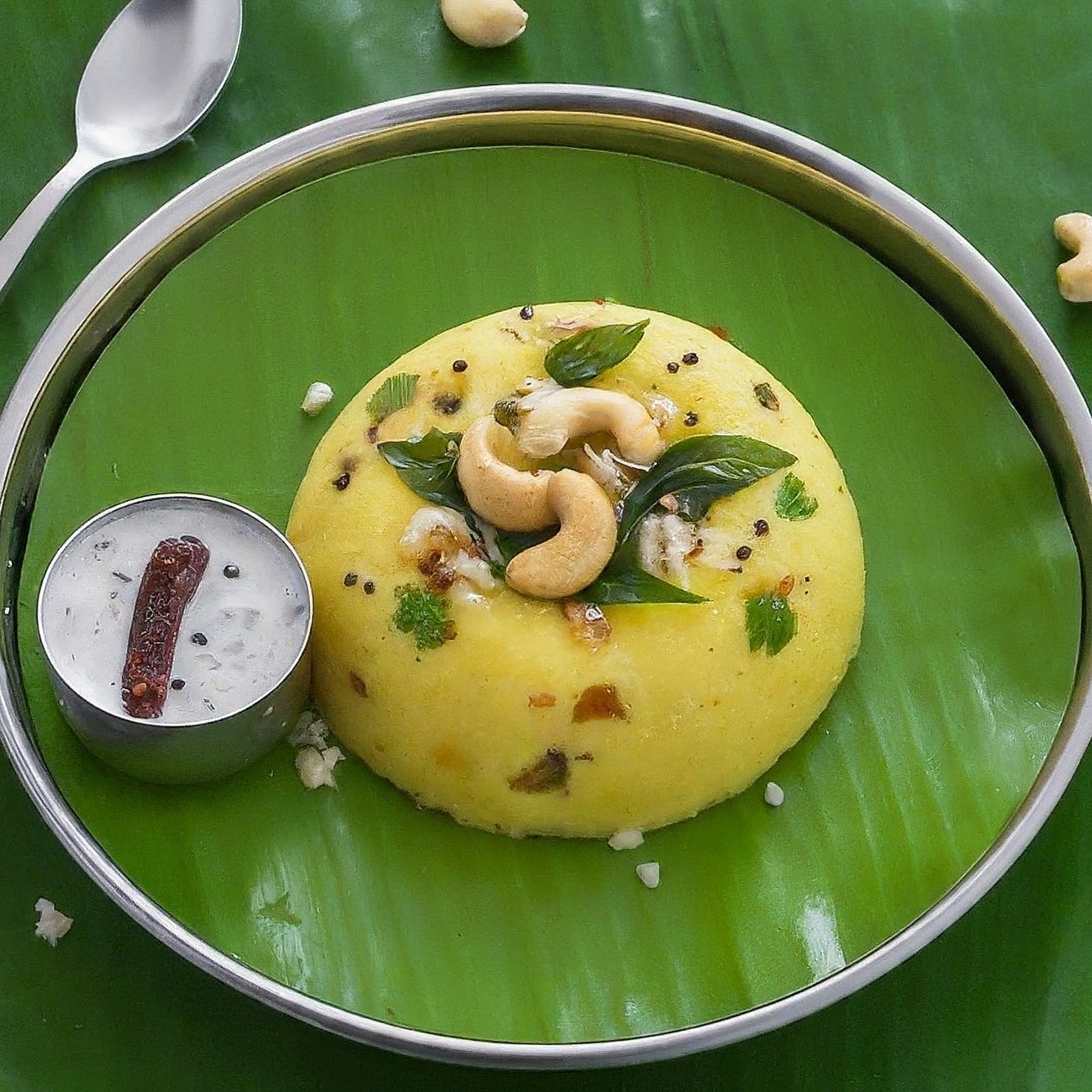 A Rava Upma breakfast served on a banana leaf with coconut chutney, cashews, and curry leaves.