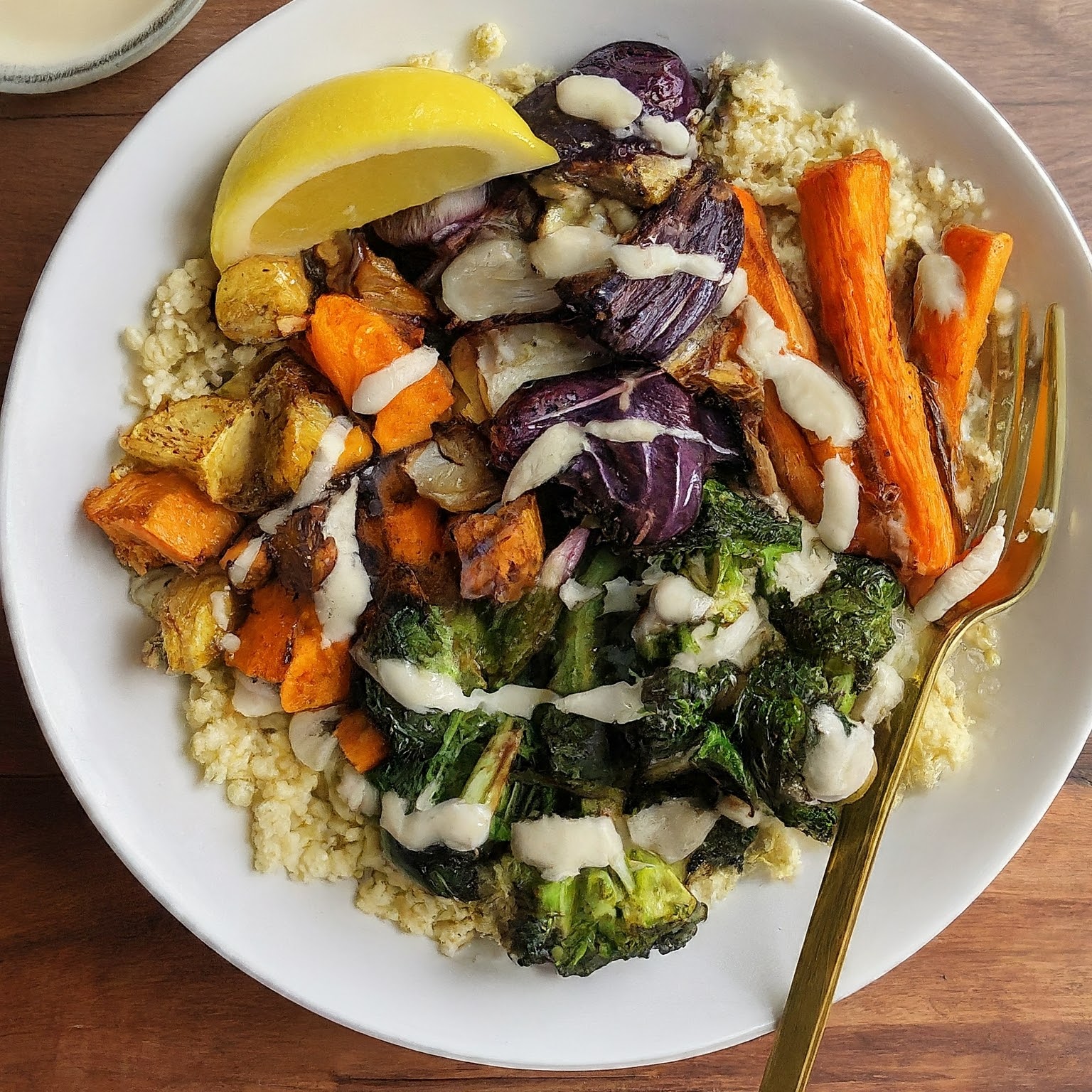 Savory Millet Veggie Bowl with colourful roasted vegetables, herbs, lemon tahini dressing, and a lemon wedge.