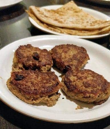 What Are the Most Famous Foods of Uttar Pradesh? 13 Tunday kebabs pan cooked with a soft finely minced texture served with flatbread on a plate