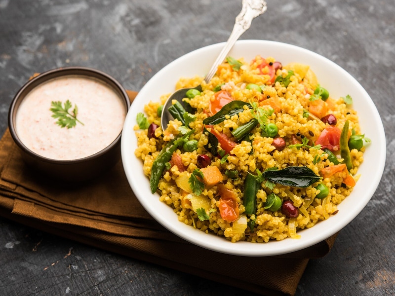 Which 10 Instant Hangover Cure Tips Should You Try Today? 11 A bowl of wheat rava vegetable upma served with a side of raita on a dark background