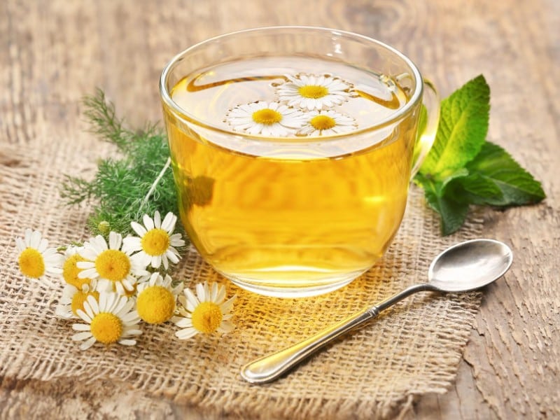 Which 10 Instant Hangover Cure Tips Should You Try Today? 7 Chamomile tea in a clear cup with flowers and a spoon on a rustic table