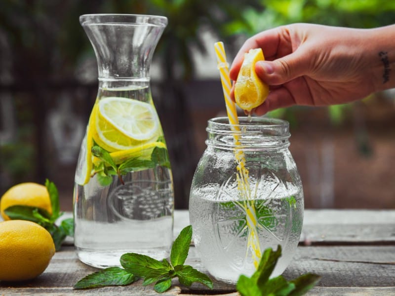Which 10 Instant Hangover Cure Tips Should You Try Today? 4 Hand squeezing a lemon wedge over a jar with mint leaves and a straw